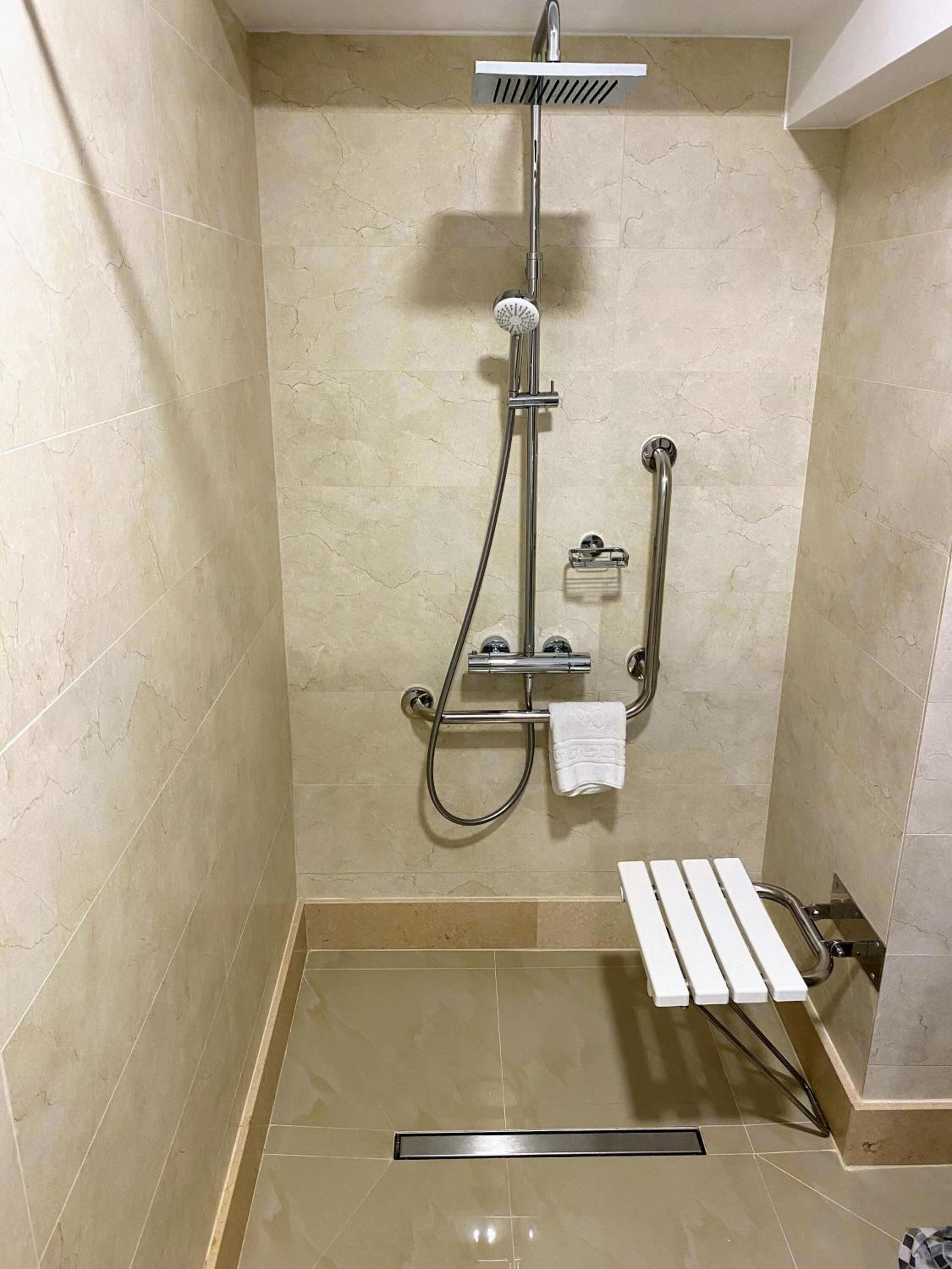 Un espacio de ducha pequeño con azulejos, un cabezal de ducha de mano, un accesorio de ducha manual y una barra de apoyo.