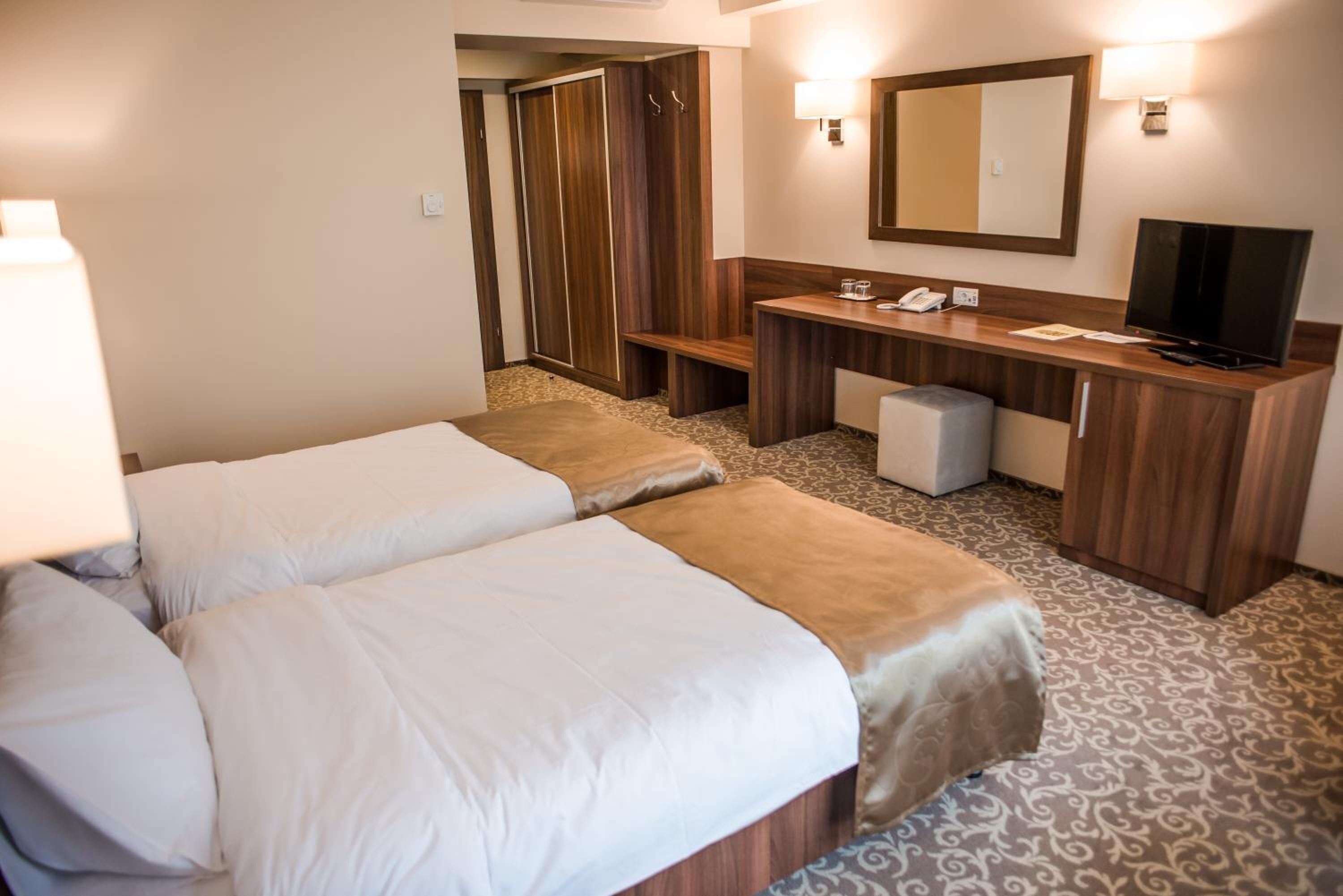 Una habitación de hotel con dos camas, un escritorio, un espejo, un televisor y un armario.