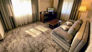 Habitación de hotel con sofá, mesa de centro, escritorio y computadora, además de cortinas.