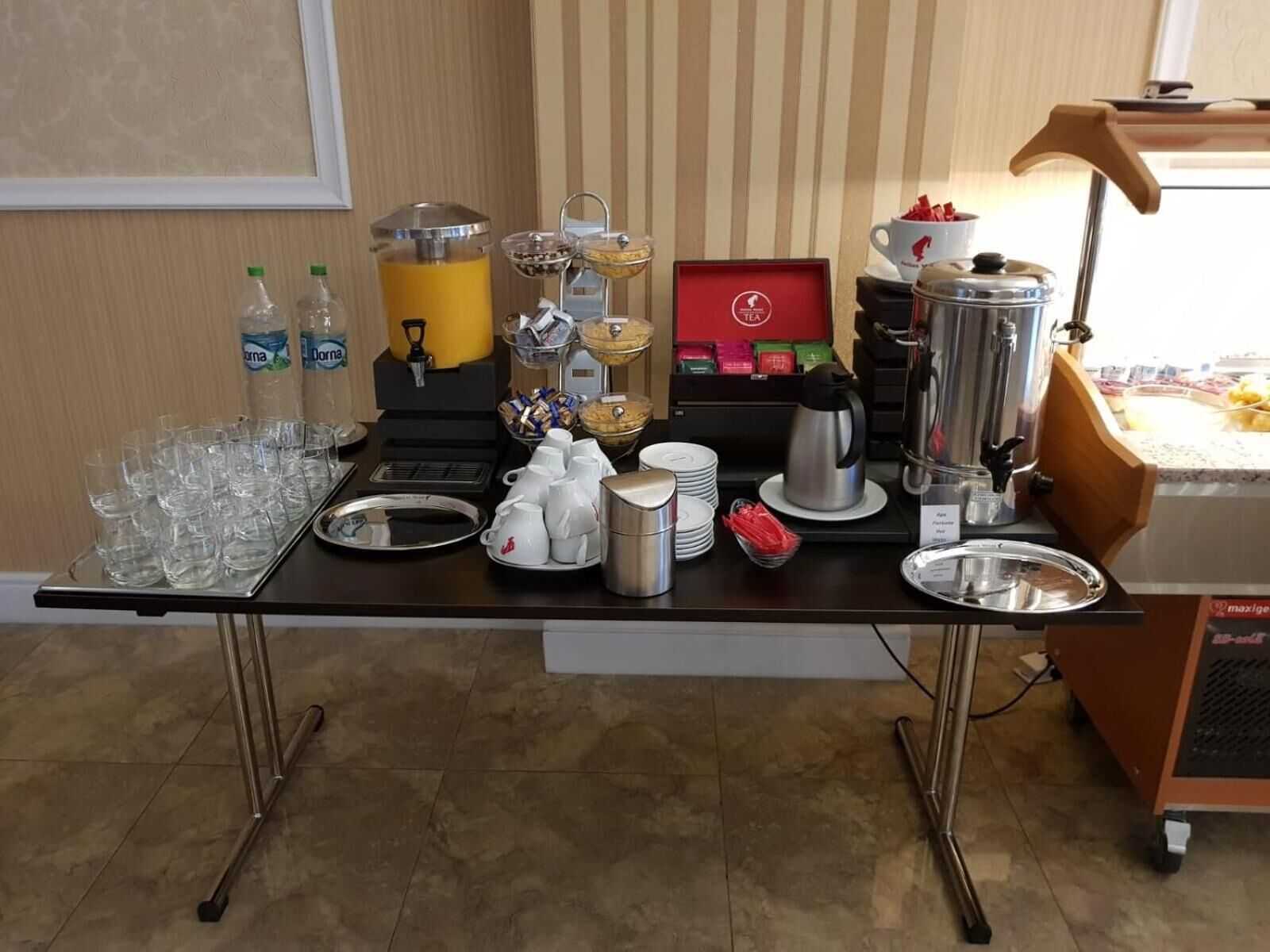 A breakfast buffet setup with various food and drink options, including juice dispensers, coffee machines, and a variety of dishes.