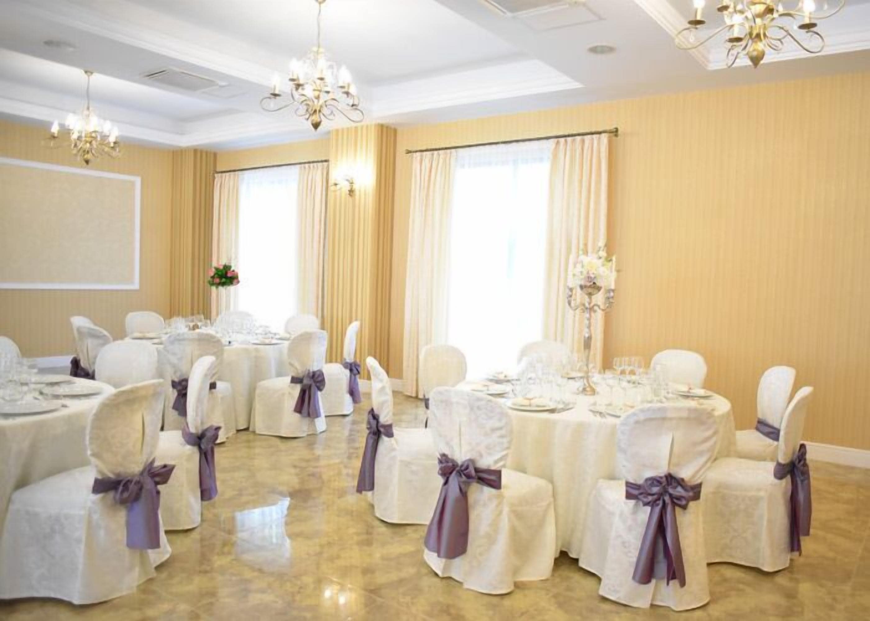 A banquet hall with round tables set for dining, white chairs with purple sashes, and chandeliers.