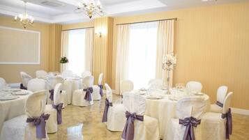 A banquet hall with round tables set for dining, white chairs with purple sashes, and chandeliers.