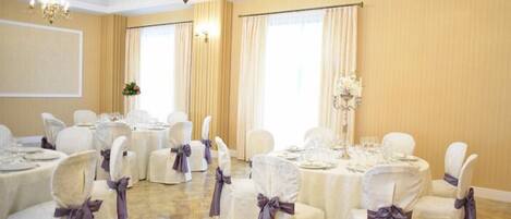 A banquet hall with round tables set for dining, white chairs with purple sashes, and chandeliers.