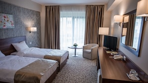 Habitación de hotel con dos camas, un escritorio con teléfono, una silla, un televisor y una mesita con una planta.