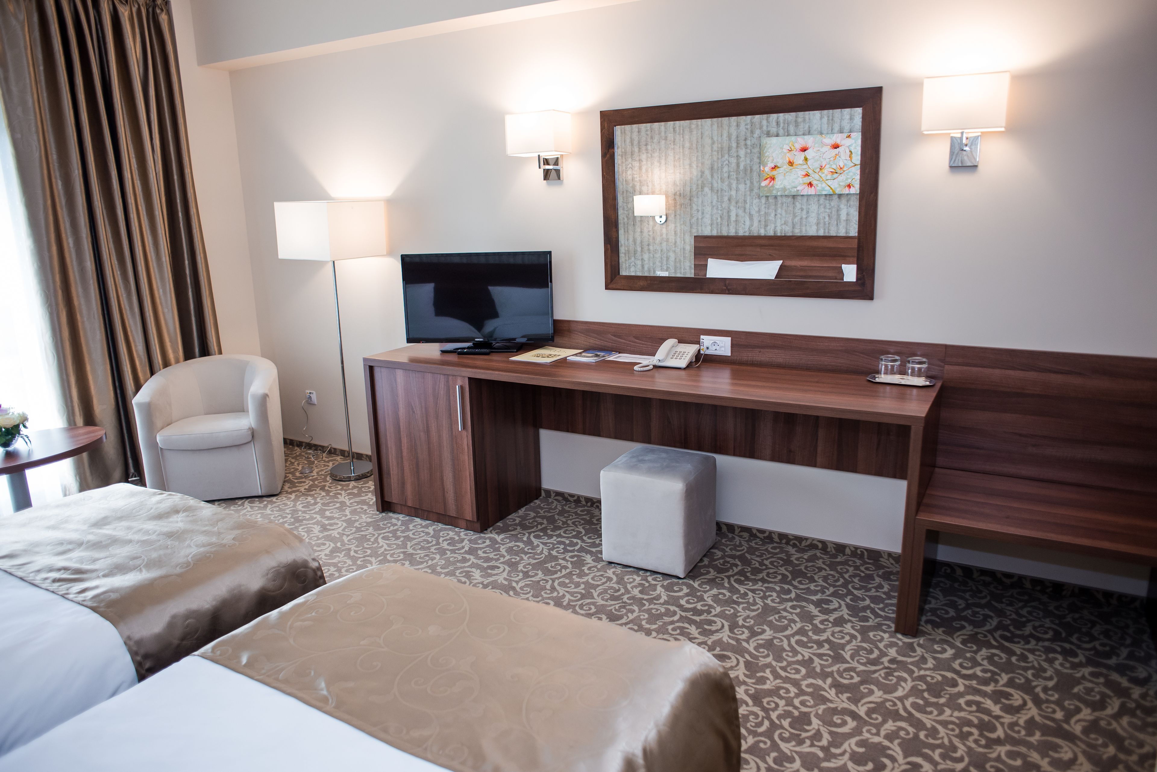 Une chambre d’hôtel avec un grand lit, un plus petit lit, un bureau avec un téléphone, une chaise, une télévision et un miroir.
