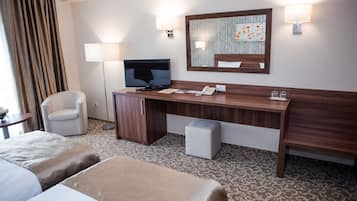 Une chambre d’hôtel avec un grand lit, un plus petit lit, un bureau avec un téléphone, une chaise, une télévision et un miroir.