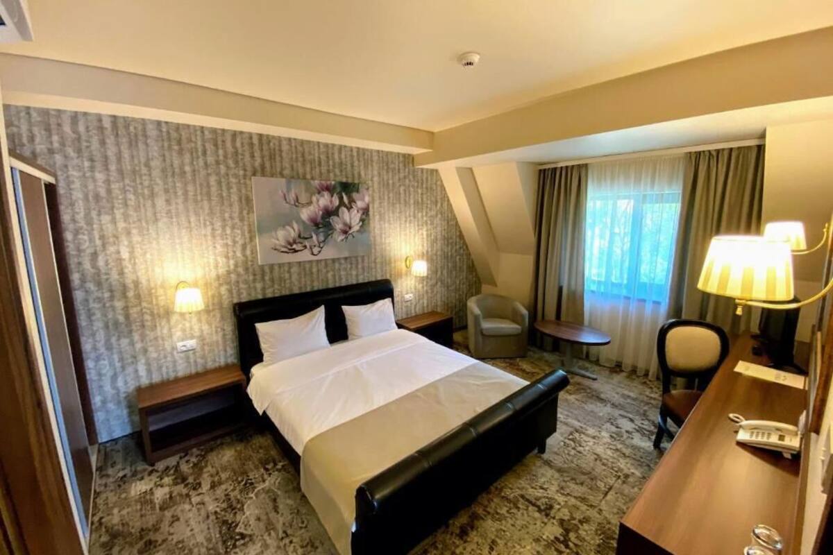 A hotel room with a large bed, a desk with a lamp, a chair, and a painting on the wall.