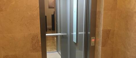 A modern elevator with a glass door and a marble floor.