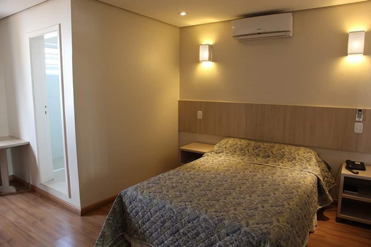 A bedroom with a bed, bedside tables, a wardrobe, and an air conditioning unit.