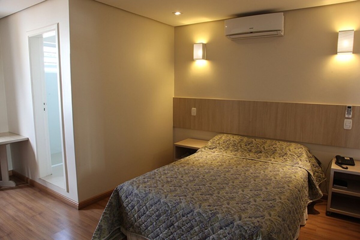 Une chambre à coucher comprenant un lit, des tables de chevet, une armoire et un appareil de climatisation.