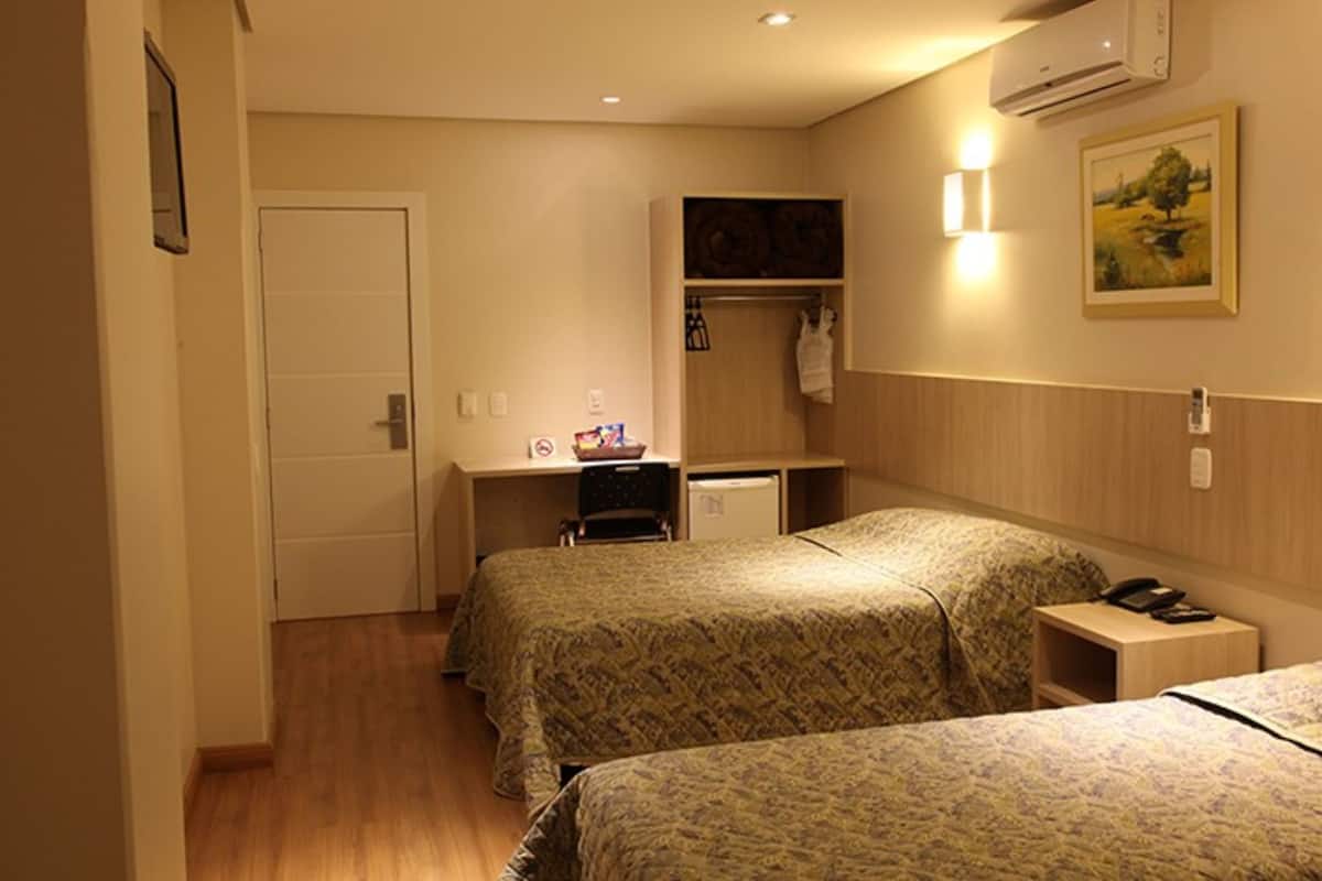 A hotel room with two beds, a desk, a chair, a small refrigerator, and a bedside table with a phone.