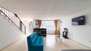 A spacious living area with a teal sofa, a grey sofa, a staircase, a flat-screen TV, and a minibar.
