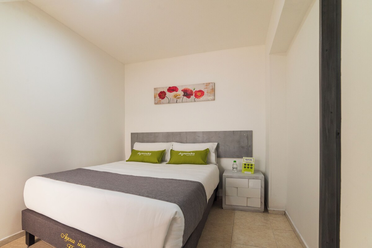 A hotel room with a bed, a nightstand, a painting, and a sign.