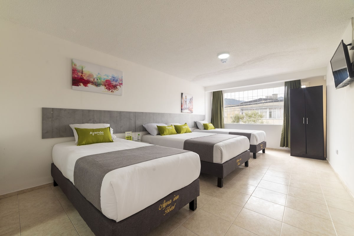 Habitación de hotel con dos camas, un ventanal grande, un cuadro en la pared y un televisor montado.