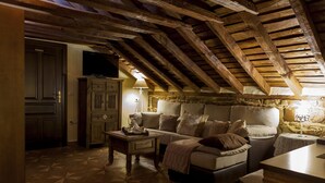 Ein gemütliches Dachzimmer mit Holzbalkendecke, einer Couch, einem Tisch und einem Fernseher.
