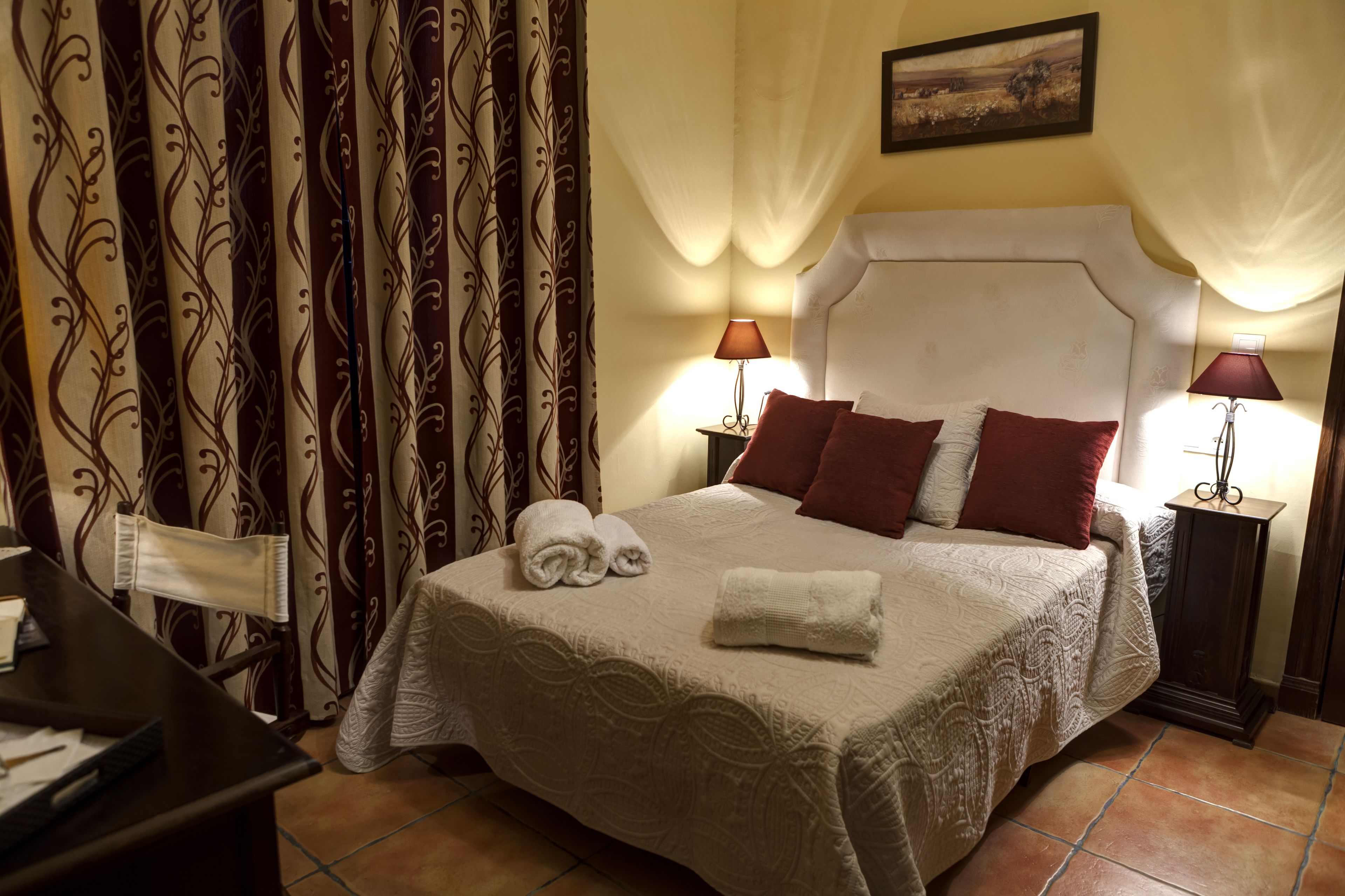 Una cama bien hecha con una colcha blanca y dos almohadas, un escritorio con una silla y cortinas con estampado floral.