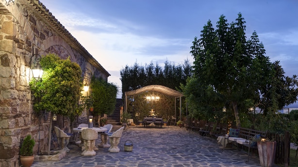 Eine Terrassenanlage im Freien mit Steinböden, Tischen, Stühlen und einer Pergola mit Beleuchtung.