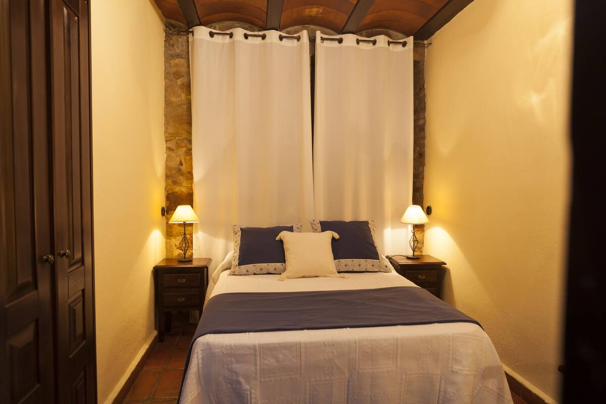 A bedroom with a bed, two bedside tables with lamps, a door, and a curtain.