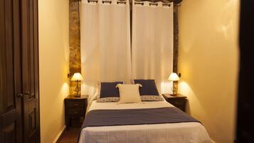 Quarto com cama, duas mesas de cabeceira com abajures, uma porta e uma cortina.
