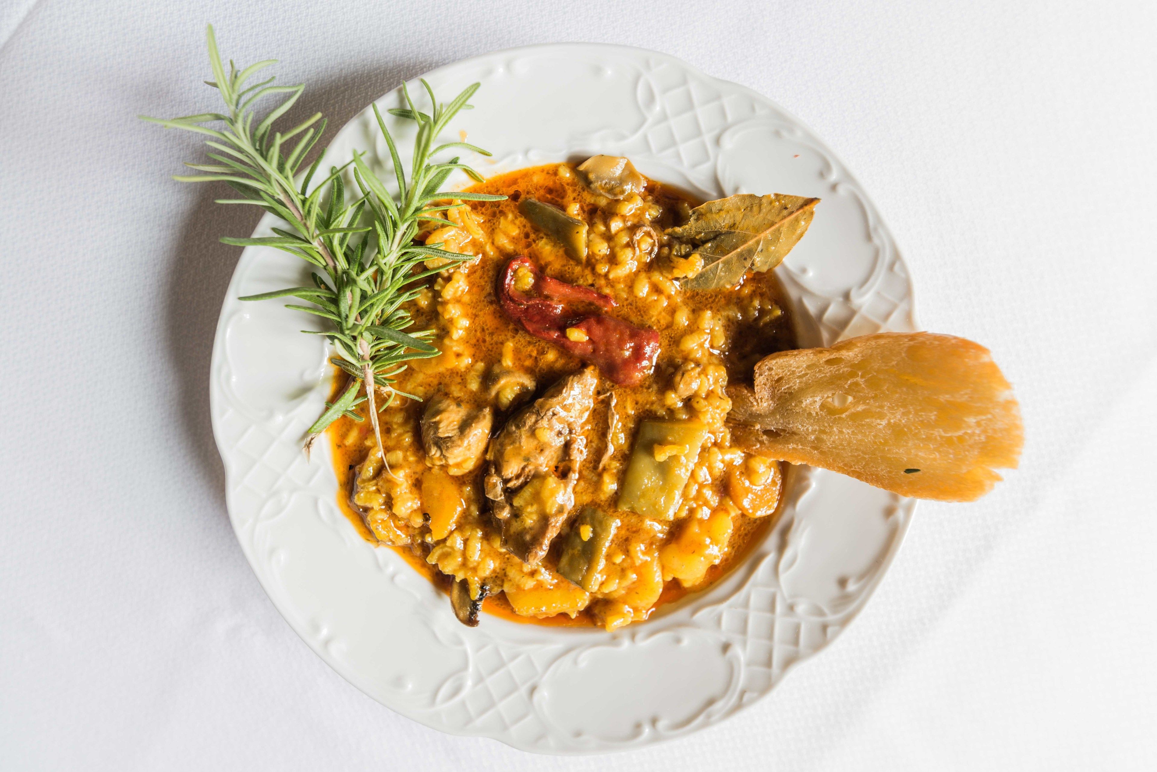 A plate of stew with vegetables and meat, garnished with rosemary, on a white plate.