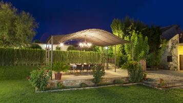 An outdoor patio area with a covered seating arrangement, stone flooring, and potted plants.