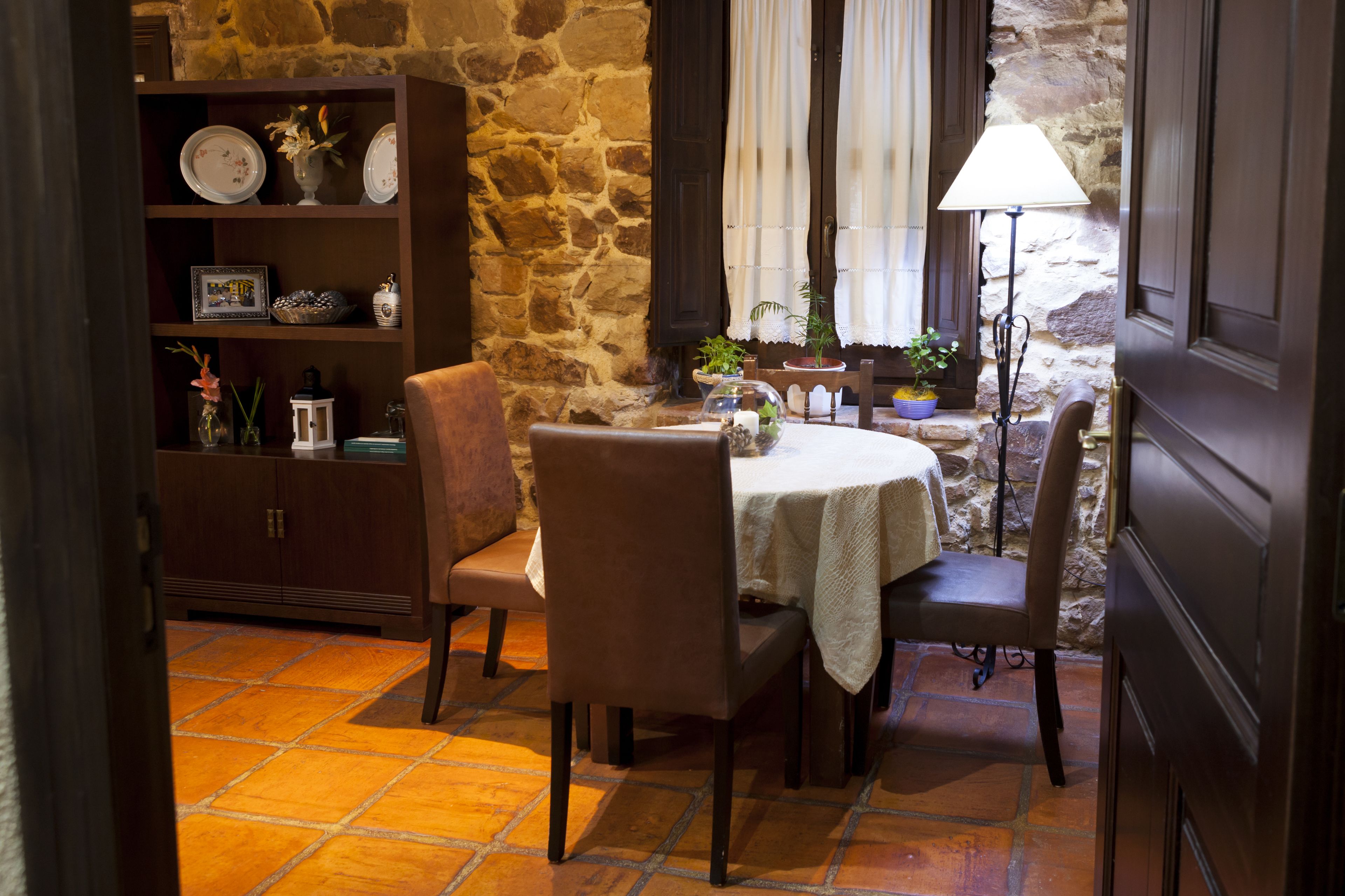 A dining area with a stone wall, a wooden cabinet with decorative items, a table with a white tablecloth, and chairs.