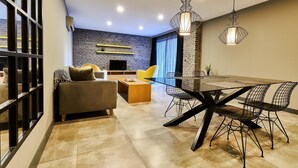 A modern living room with a sofa, a dining table with chairs, a TV, and a brick wall. - Loft 1502 (Antalya)