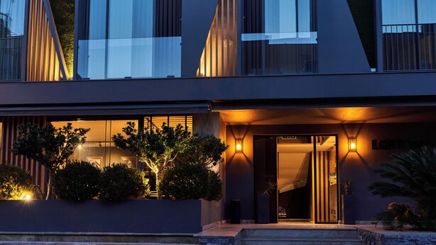 A modern building with large windows, a well-lit entrance, and a landscaped area with plants. - Loft 1502 (Antalya)