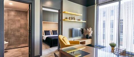 A modern hotel room with a glass partition separating the living area from the bedroom.