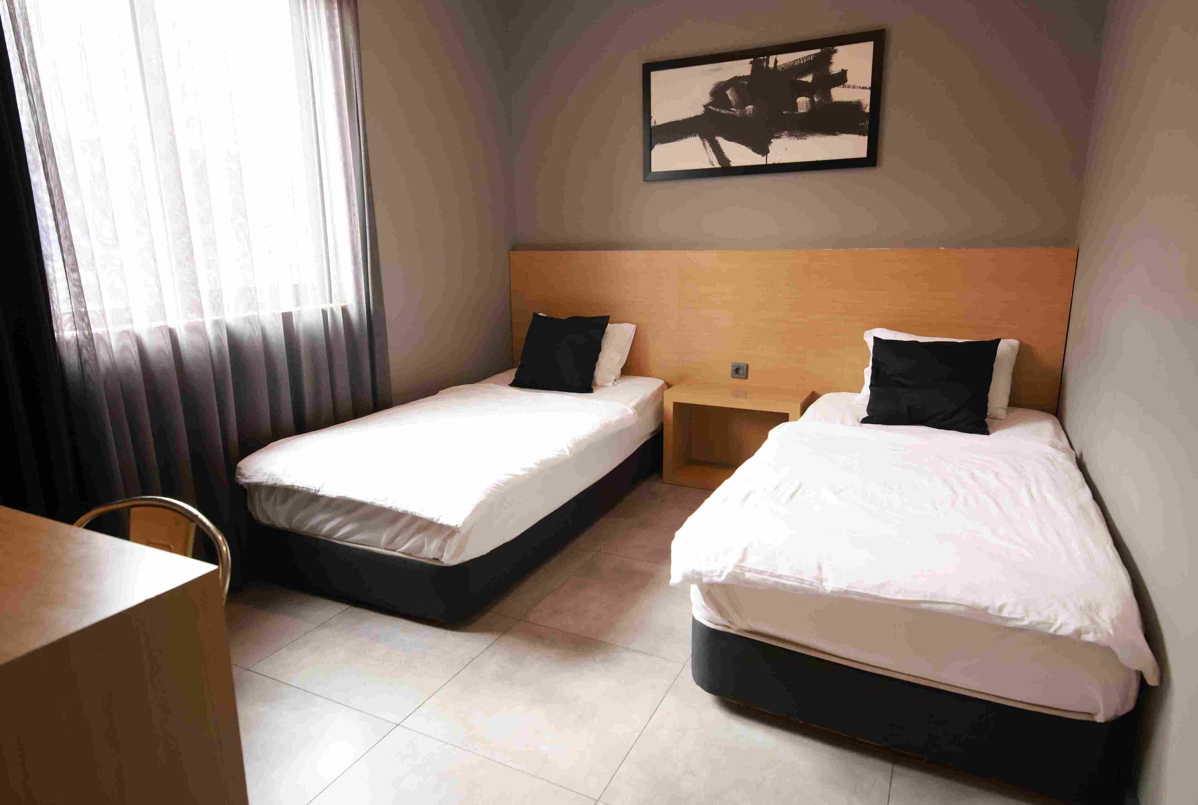 A hotel room with two single beds, a wooden headboard, a small table, and a chair.