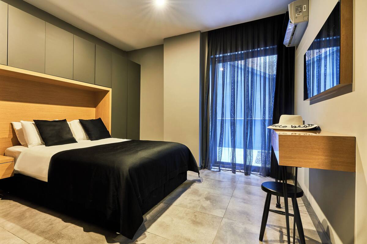 Una habitación de hotel moderna con una cama grande, un escritorio y una ventana con cortinas traslúcidas.