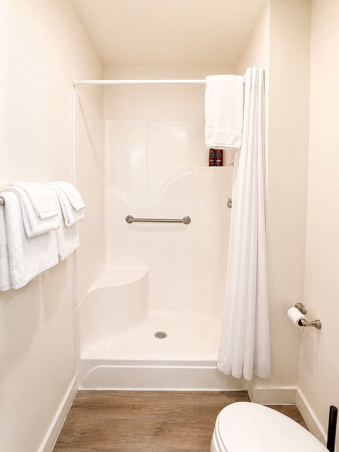 A small, white bathroom with a shower, a toilet, and a towel rack.