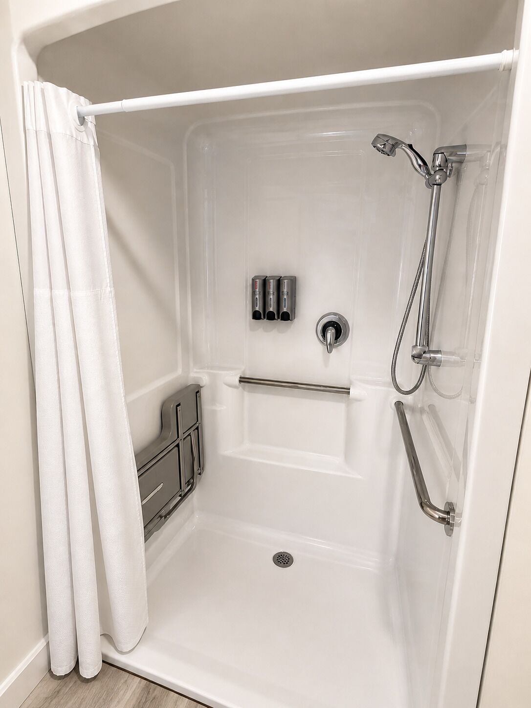 A white shower stall with a handheld showerhead, a handheld shower control, and a grab bar.