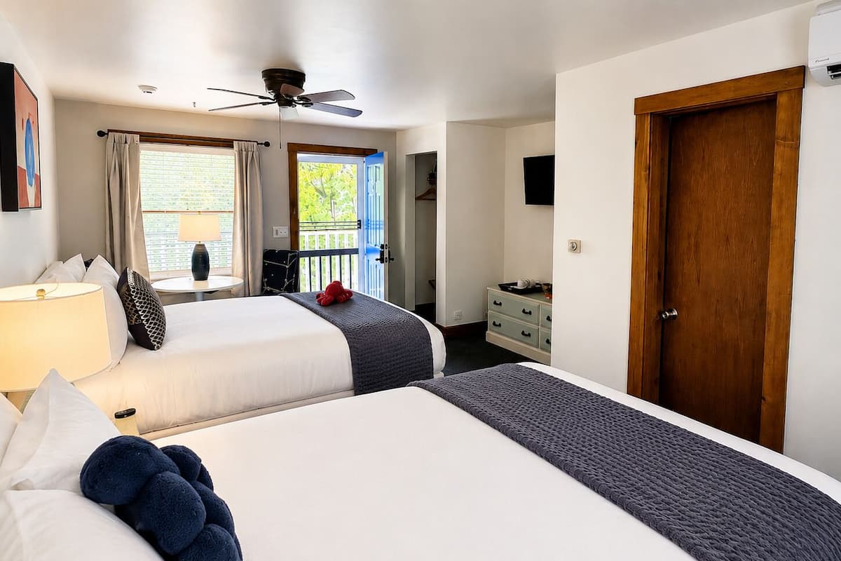 Habitación de hotel con dos camas, ventilador de techo, balcón, cómoda y una puerta.