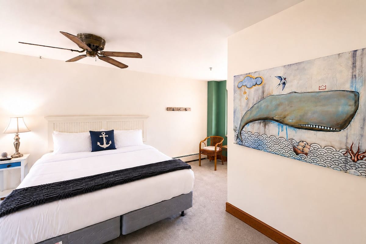 Un dormitorio con cama, ventilador de techo, una silla y un cuadro en la pared.