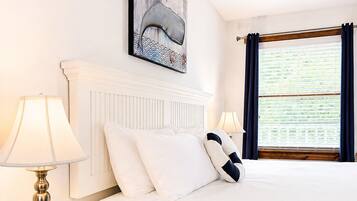 A hotel room with a bed, a nightstand, a lamp, a ceiling fan, a window with curtains, and a painting on the wall.