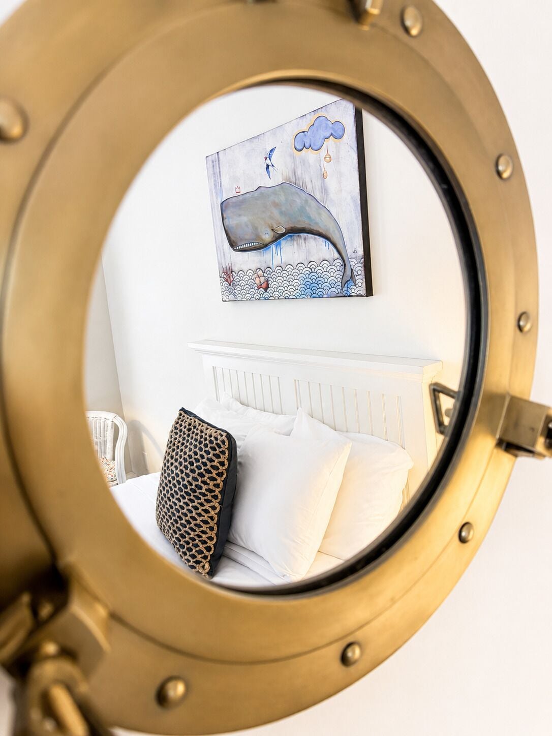 Uno specchio rotondo che riflette un letto, cuscini e un quadro a parete raffigurante una balena.
