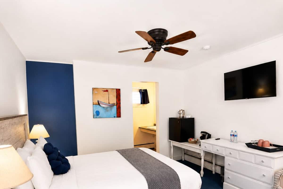 Una habitación de hotel con cama, escritorio, silla, televisor y ventilador de techo.
