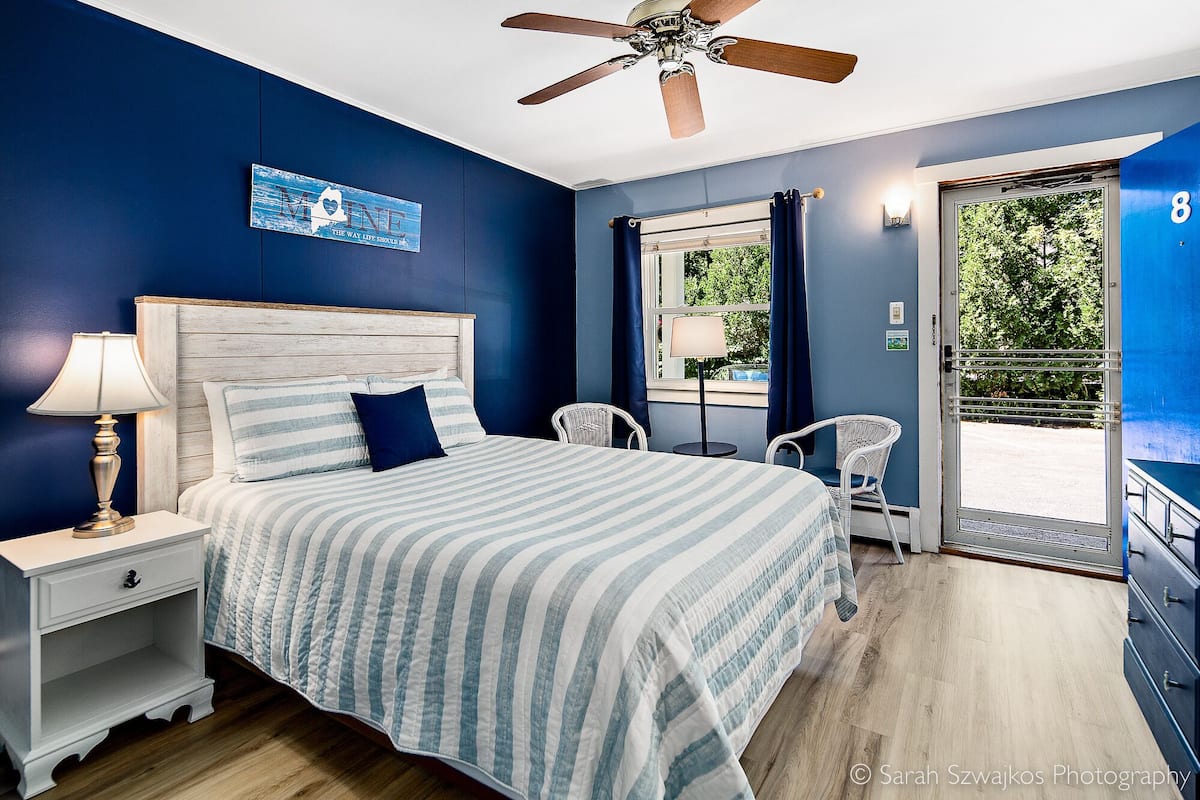 Un dormitorio con cama, mesita de noche, lámpara y ventilador de techo.