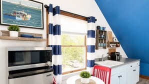 Eine kleine Küche mit Kühlschrank, Mikrowelle und Spüle. Ein Esstisch mit Stühlen und ein Fenster mit Vorhängen.