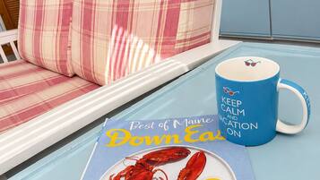 A dining table with a lobster, lemon, and utensils, a blue mug with text, and a plaid sofa in a room with a window and kitchen in the background.