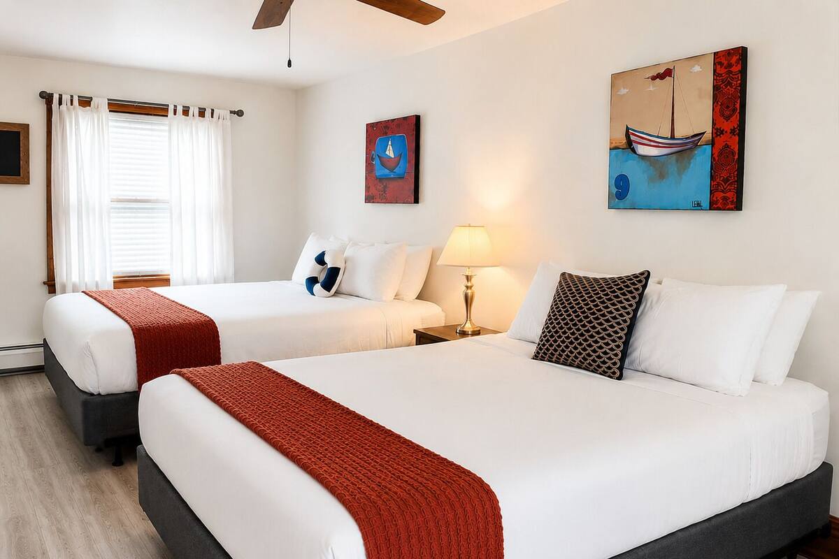 Una habitación de hotel con dos camas, una mesita de noche, una lámpara y obras de arte en las paredes.