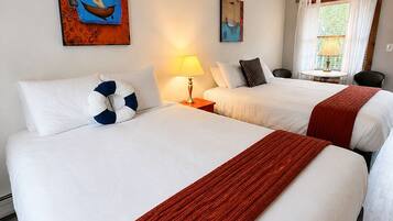A hotel room with two beds, a ceiling fan, a window with curtains, and artwork on the walls.