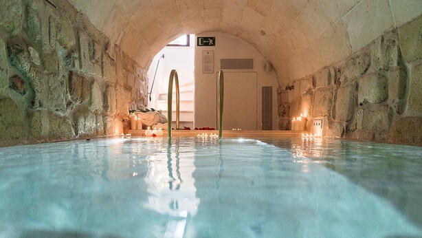 An indoor swimming pool with stone walls, a clear ceiling, and candles on the floor.