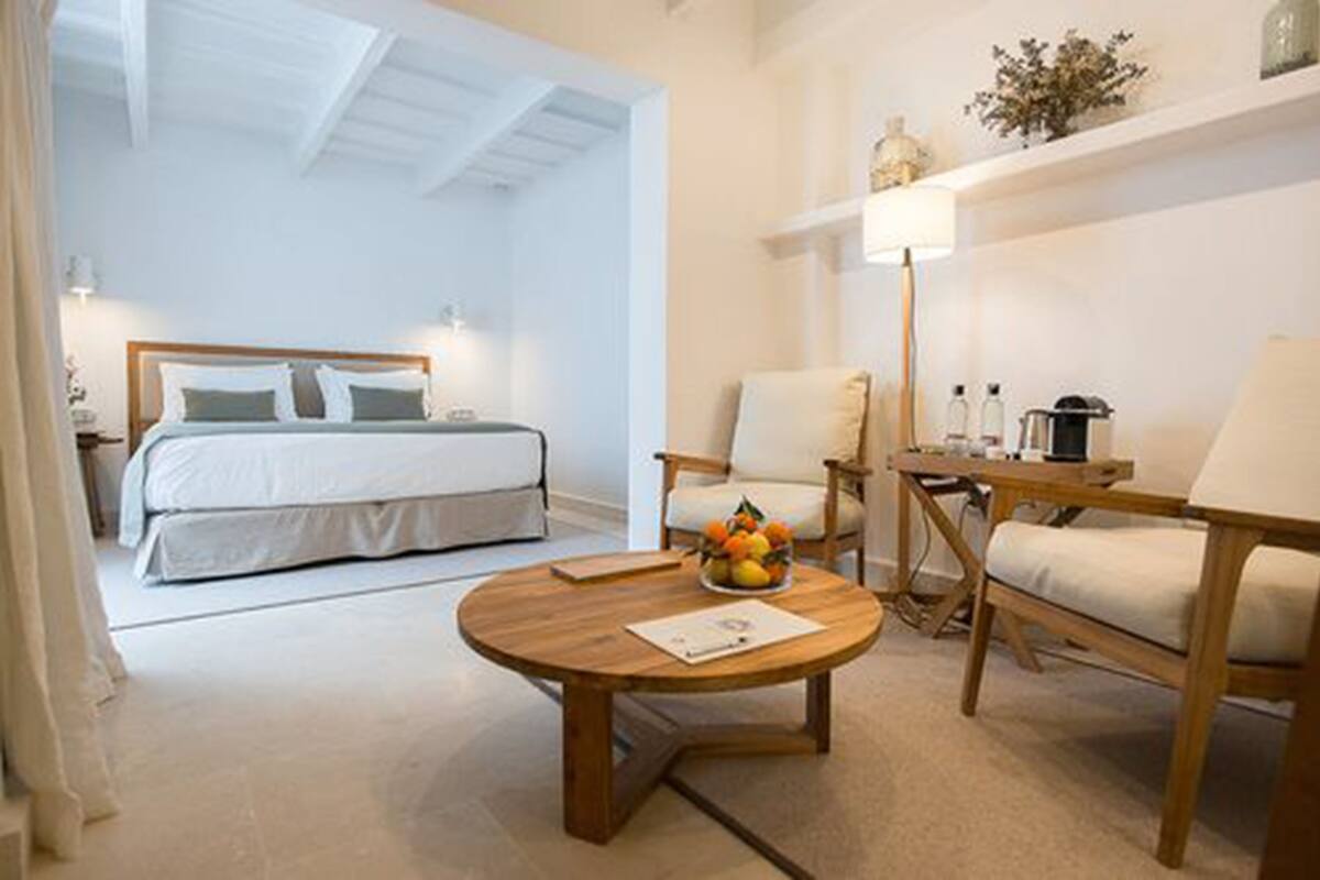 A bedroom with a bed, bedside table, and a round wooden table with fruit.