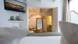 A hotel room with a bed, a television mounted on the wall, a wooden chair, a small table with fruit, and a mirror.