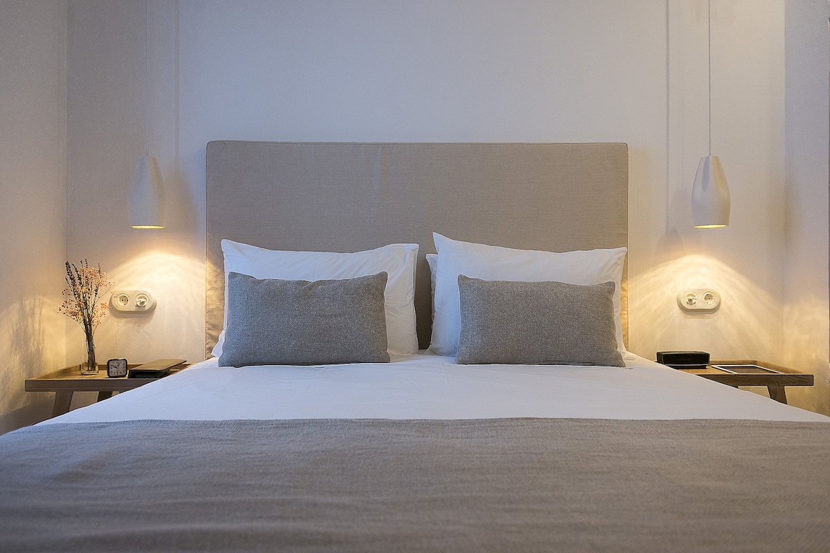 A neatly made bed with a headboard, two bedside tables, and wall-mounted lamps.