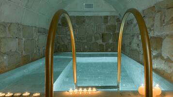 A stone-walled spa with a hot tub, candle-lit area, and a stone floor.