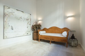 Una habitación con un sofá de madera, un cuadro abstracto grande, un florero con flores e iluminación empotrada en la pared.