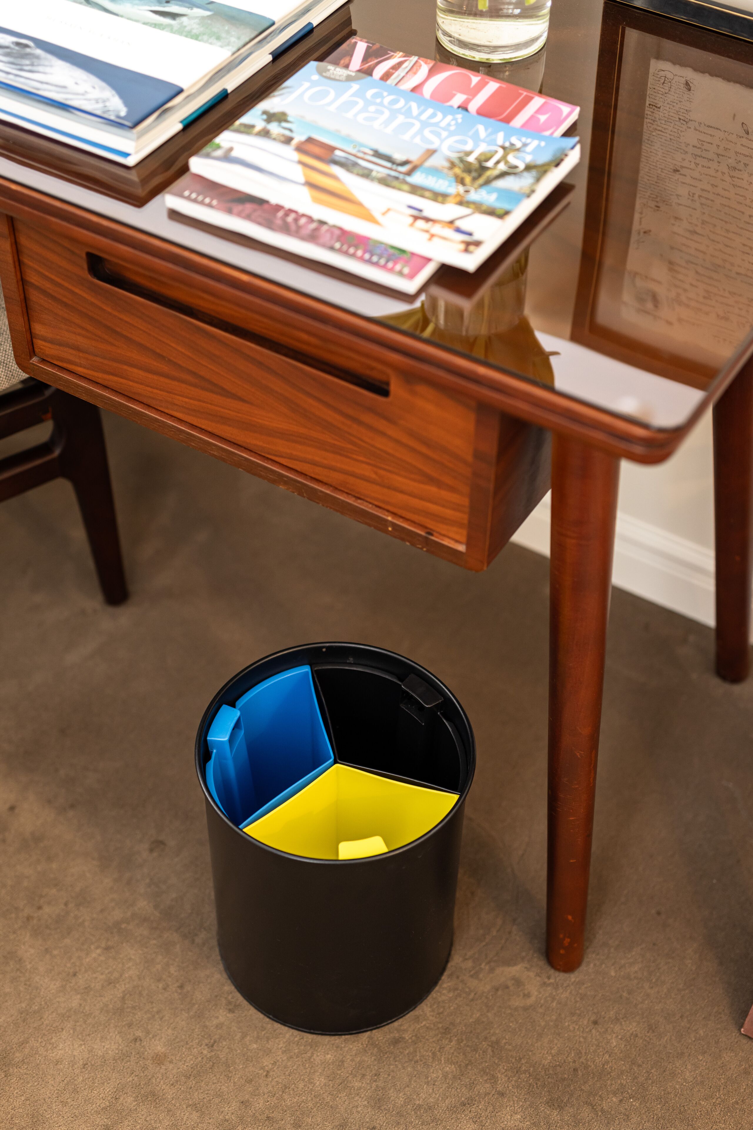 A desk with a drawer, a magazine, and a black container with yellow and blue sections.
